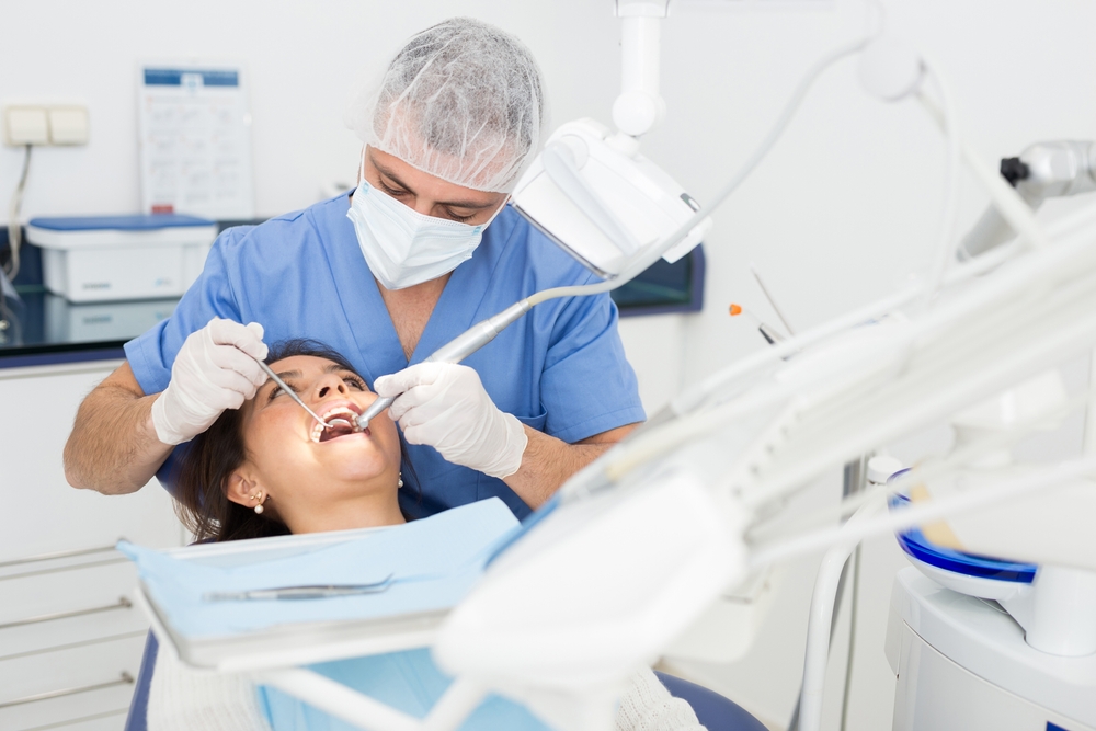 Practitioner male dentist drilling tooth to female patient in dental studio