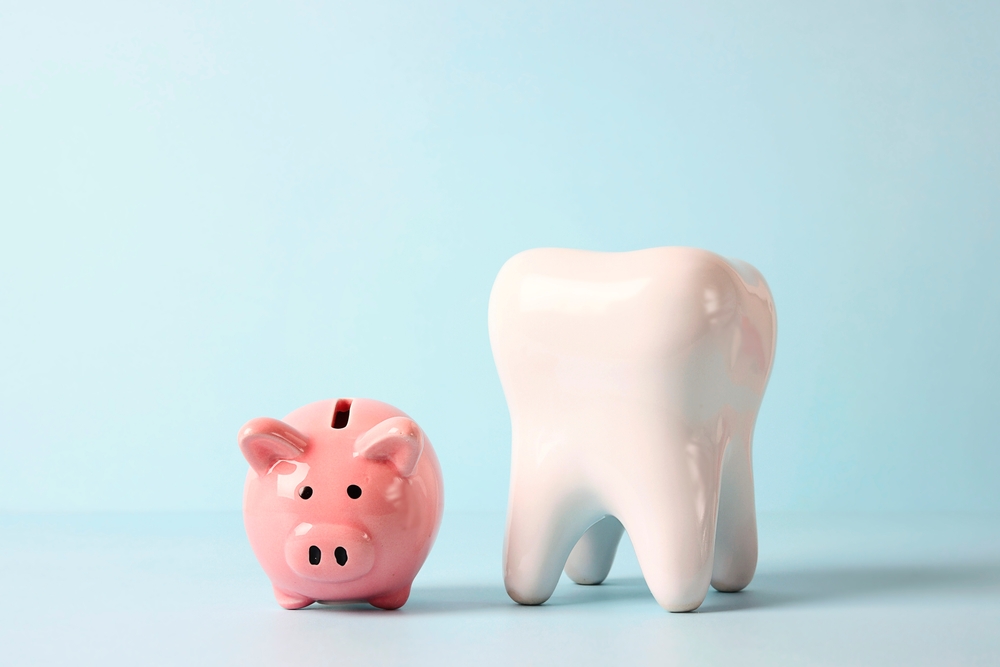 Pink piggy bank with tooth model on blue background.