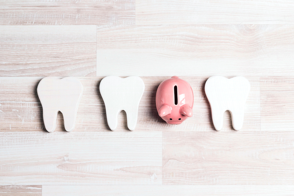 Pink piggy bank with teeth on a light wooden background.